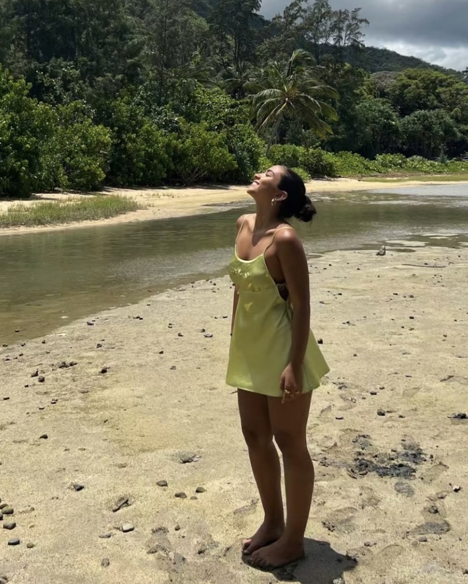 Girl standing on beach in green slip dress with face turned up toward the sun