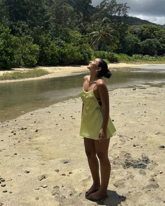 Girl standing on beach in green slip dress with face turned up toward the sun
