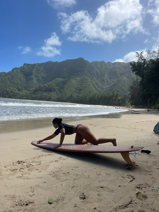 Girl waxing a maroon surf board while on the beach