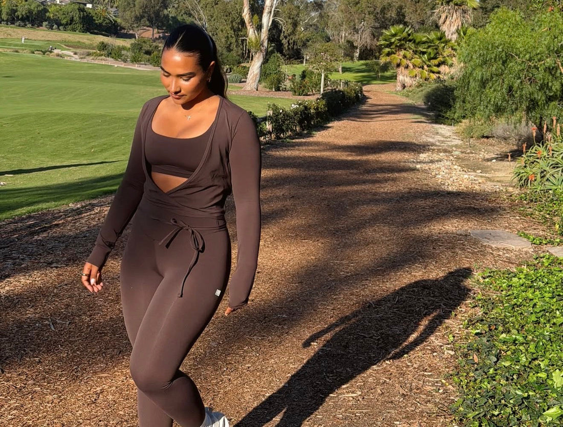 Sienna Mae Gomez walking outdoors in a brown workout set on a sunlit path, part of her daily movement and fitness routine.