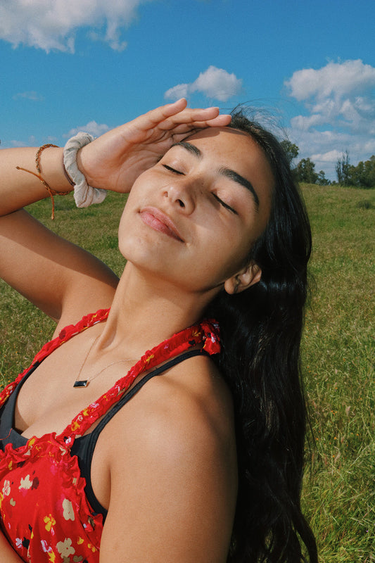 Girl in a field with a red dress and a hand on her face shielding the sun