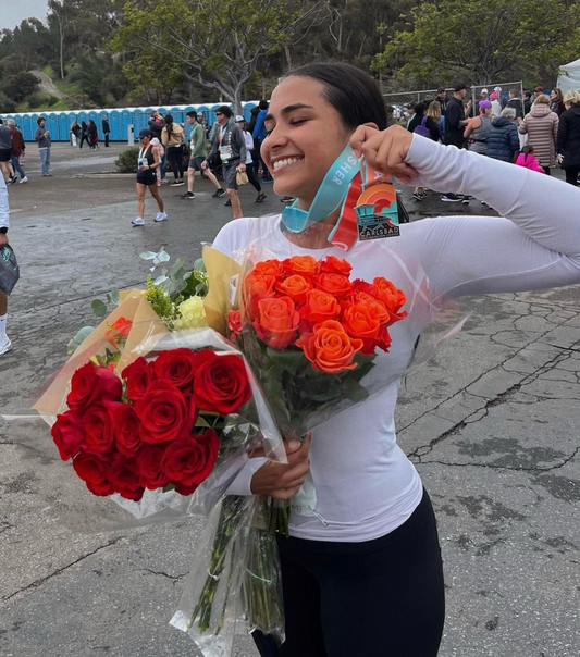 Girl holding flowers and showing a gold medal while wearing a long sleeve white tee and black active pants