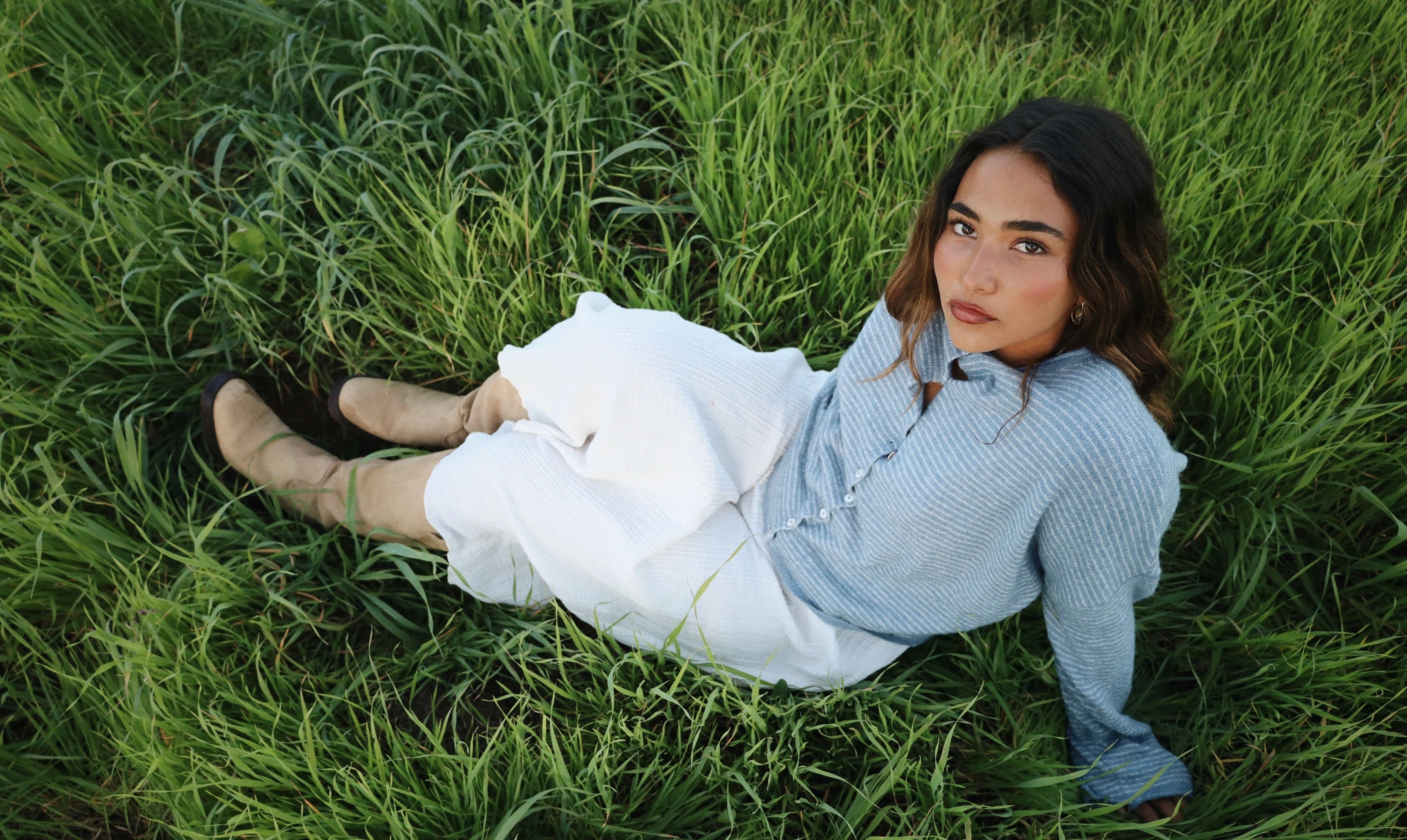 Sienna Gomez lying on grass wearing a white skirt and blue sweater
