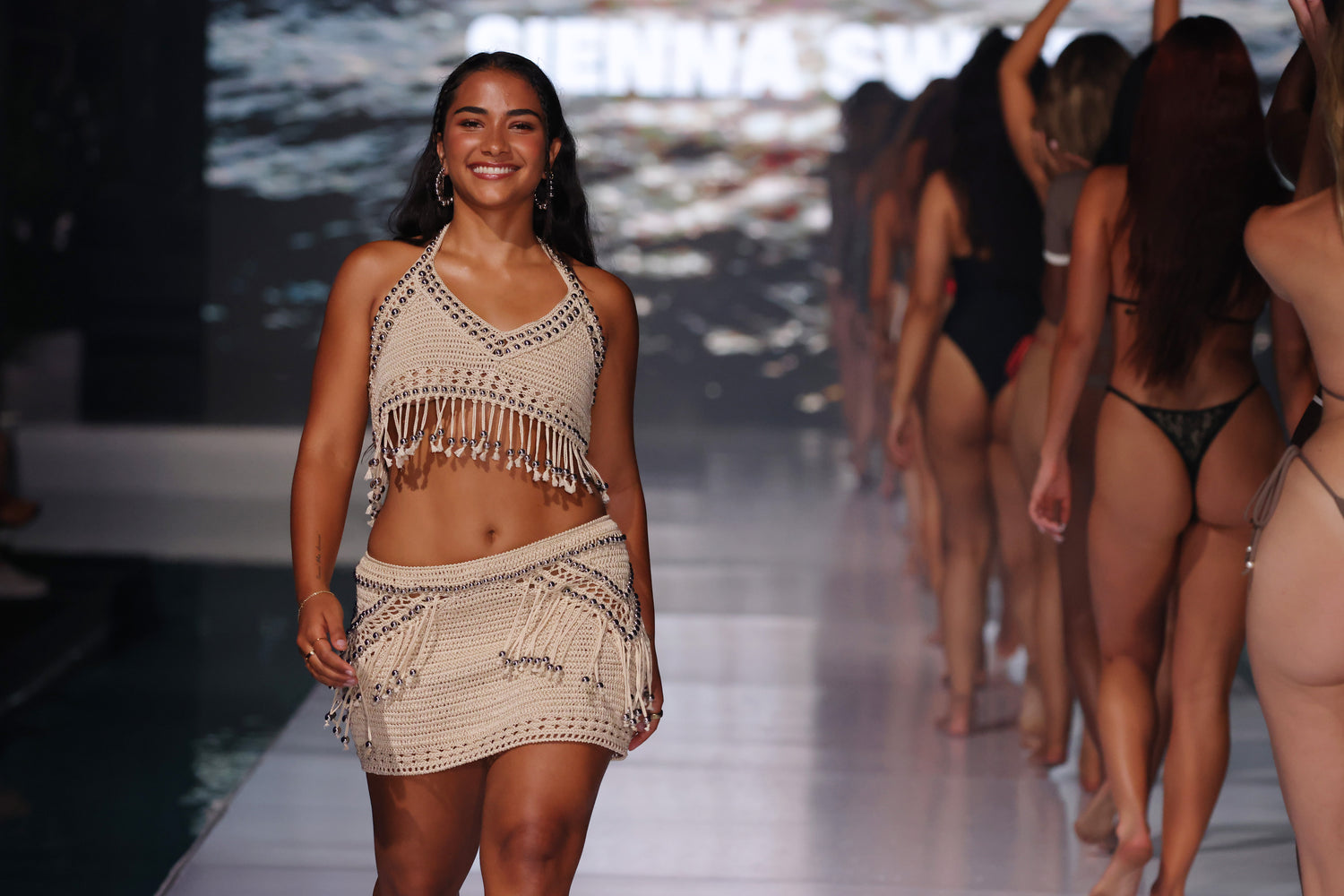 Sienna walking on the Miami Swim Week runway wearing a beach-style outfit with fringe details.