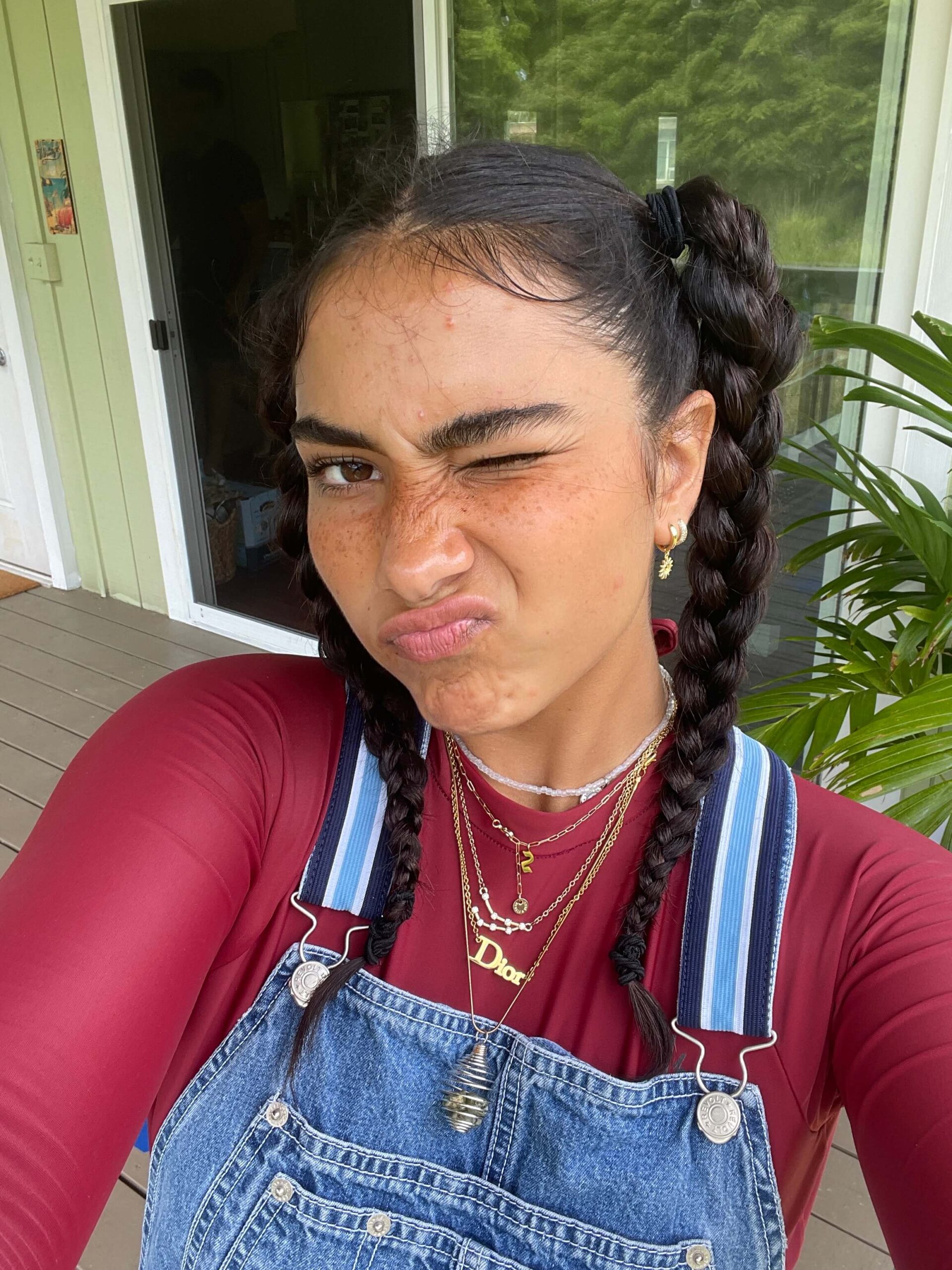 Girl with two braids, freckles, wearing overalls and a red long sleeve shirt with gold necklaces around her neck