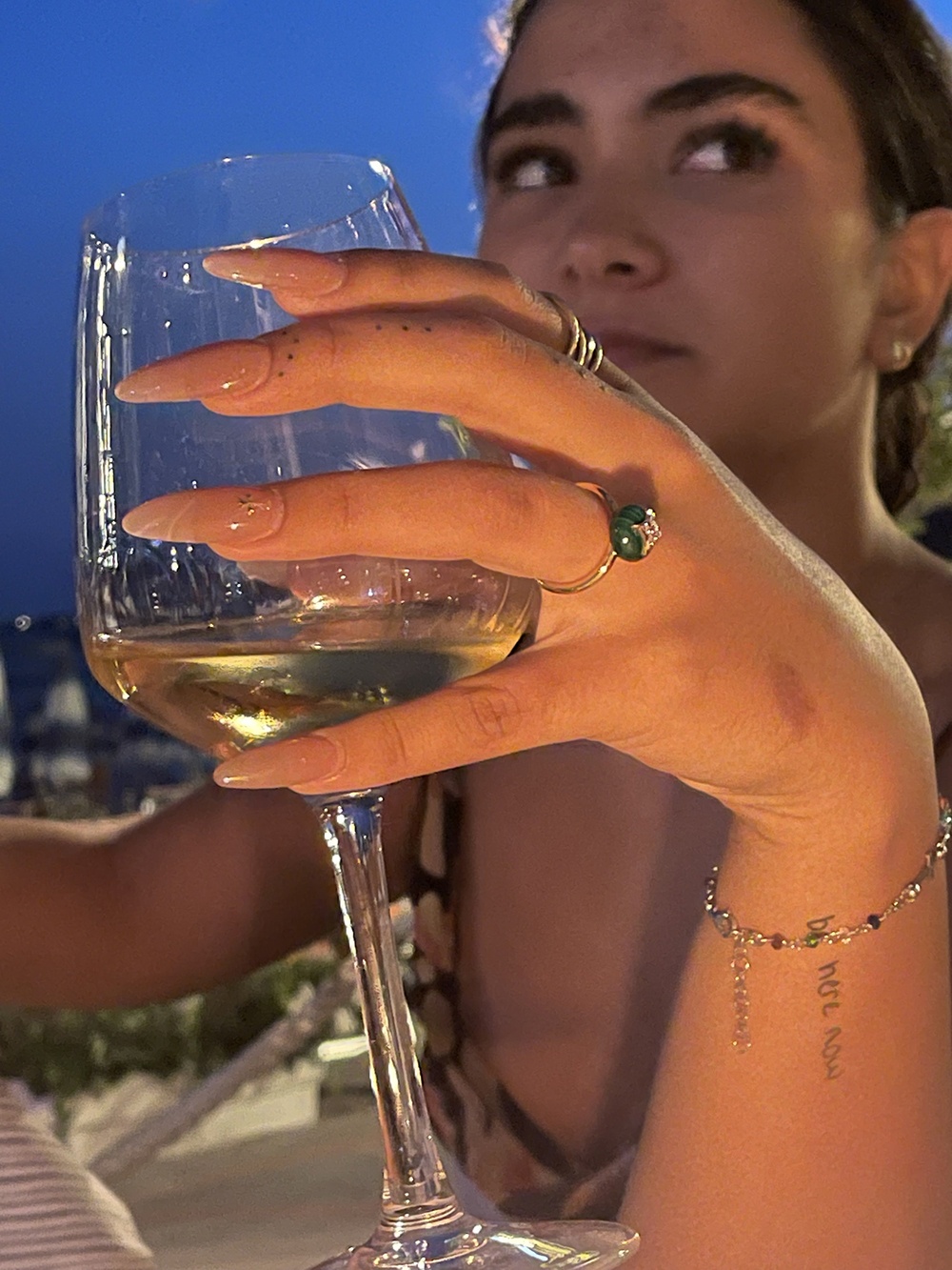 Hand holding wine glass with rings on, white wine