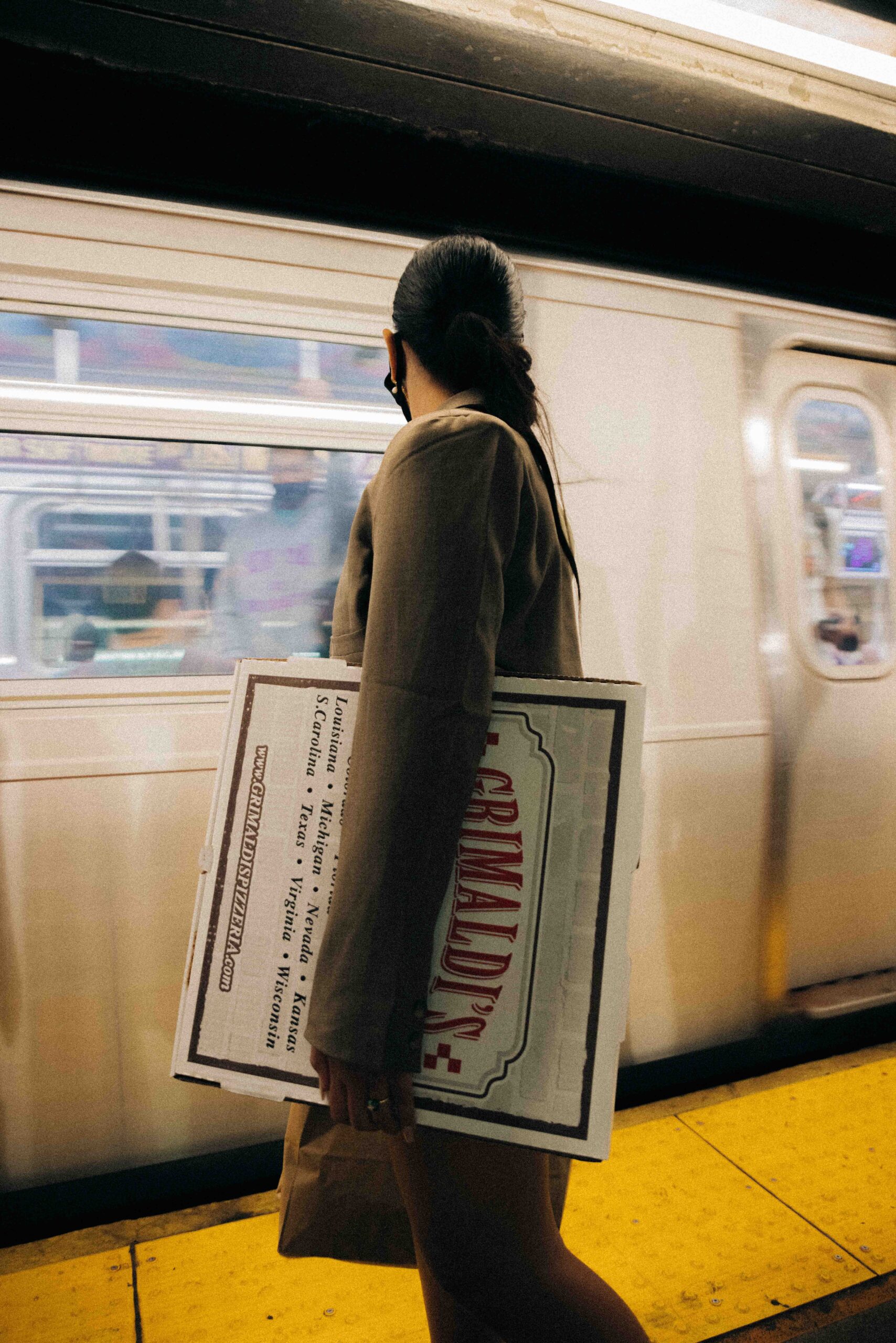 Girl holding pizza box in front of Subway Car