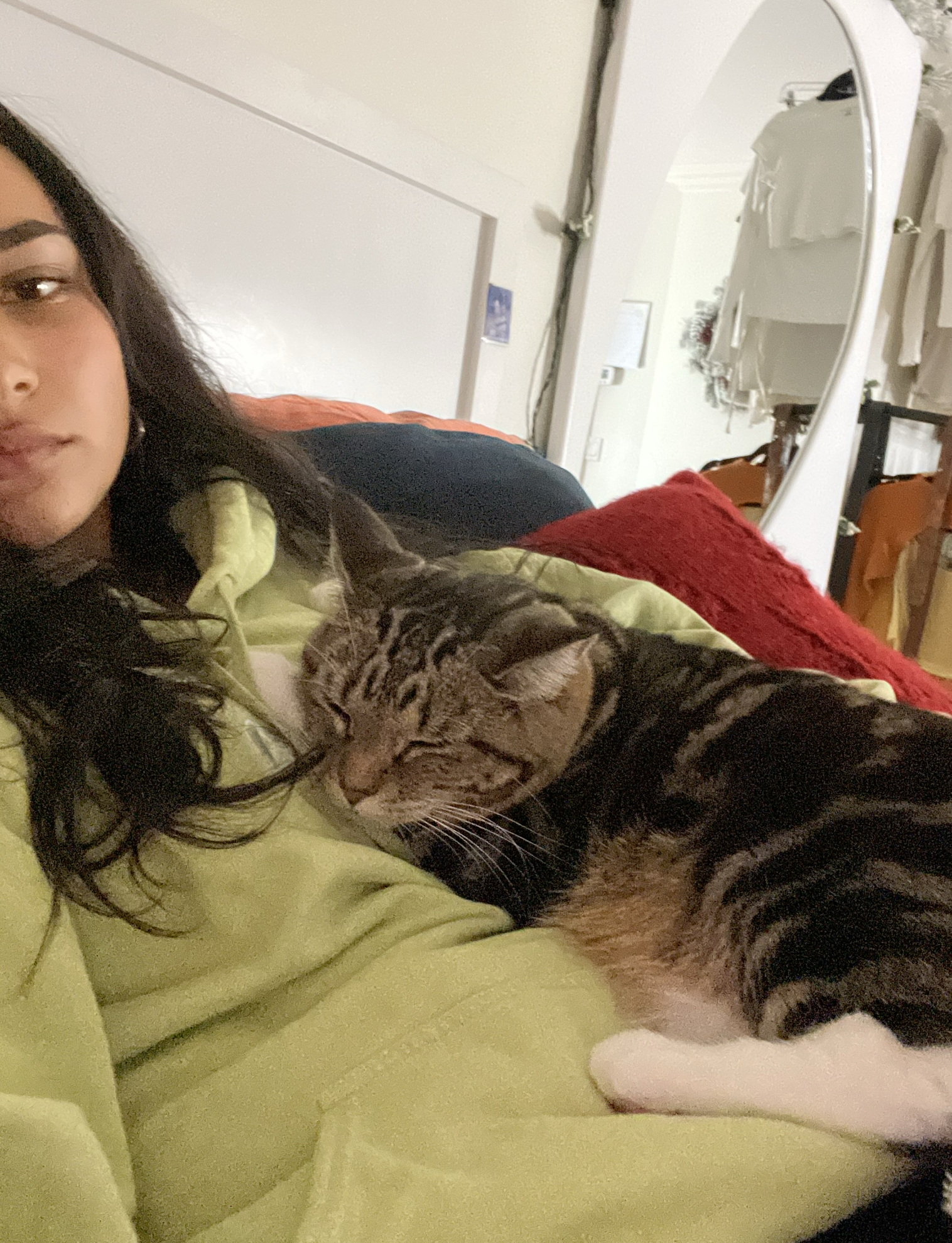 Sienna Mae Gomez with her pet cat laying across her chest; girl in green sweatshirt with long black hair and striped cat lounging on her chest