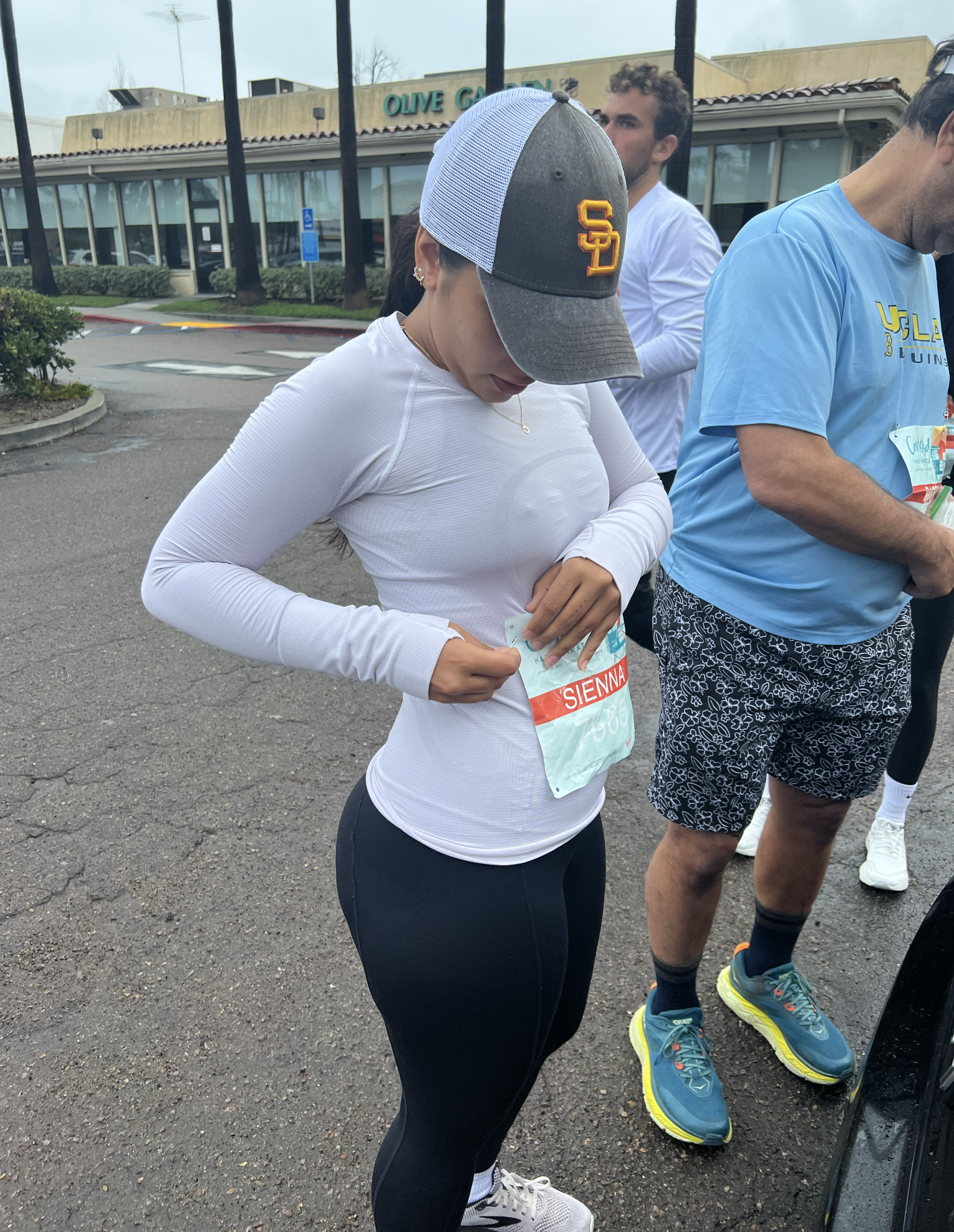 Girl in white long sleeve top and San Diego baseball cap pinning a race bib to her shirt in preparation for a marathon
