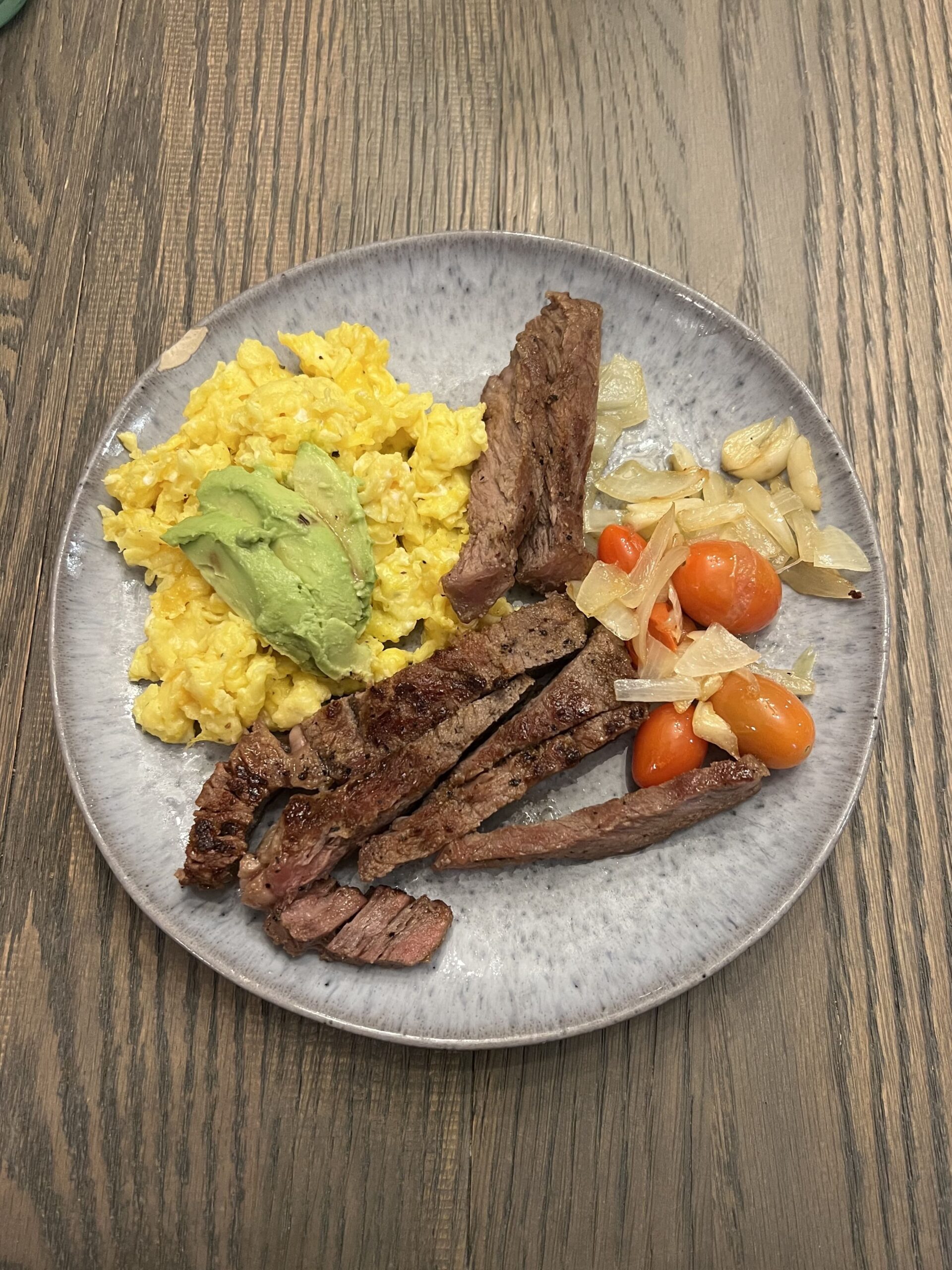 Steak and egg breakfast plate with avocado, scrambled eggs, steak well done, tomatoes and onions