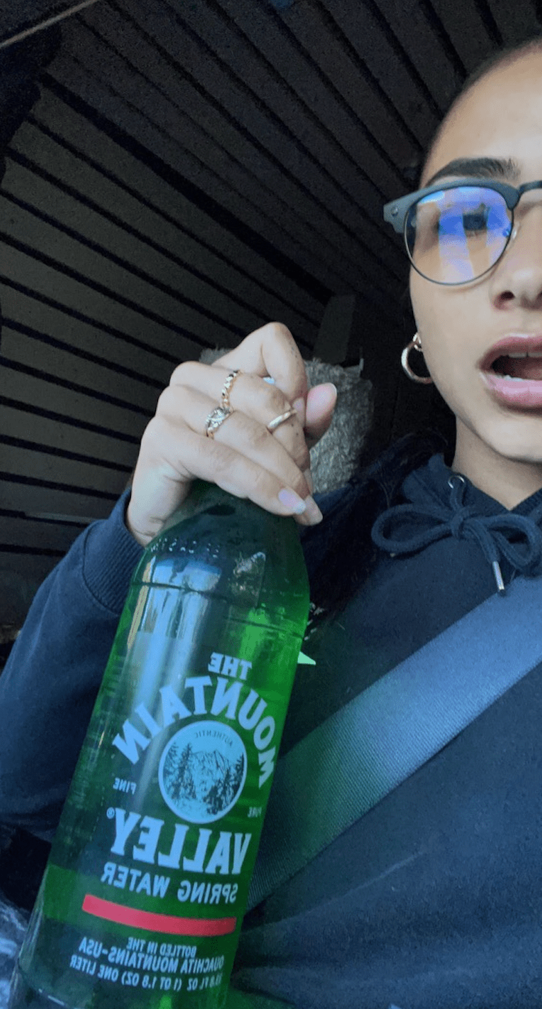 Girl in glasses holding green glass bottle of spring water from mountain valley