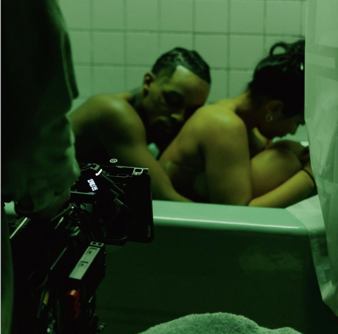Girl and boy sitting together in bathtub, where we see a camera in bottom left foreground to show a behind the scenes look at production