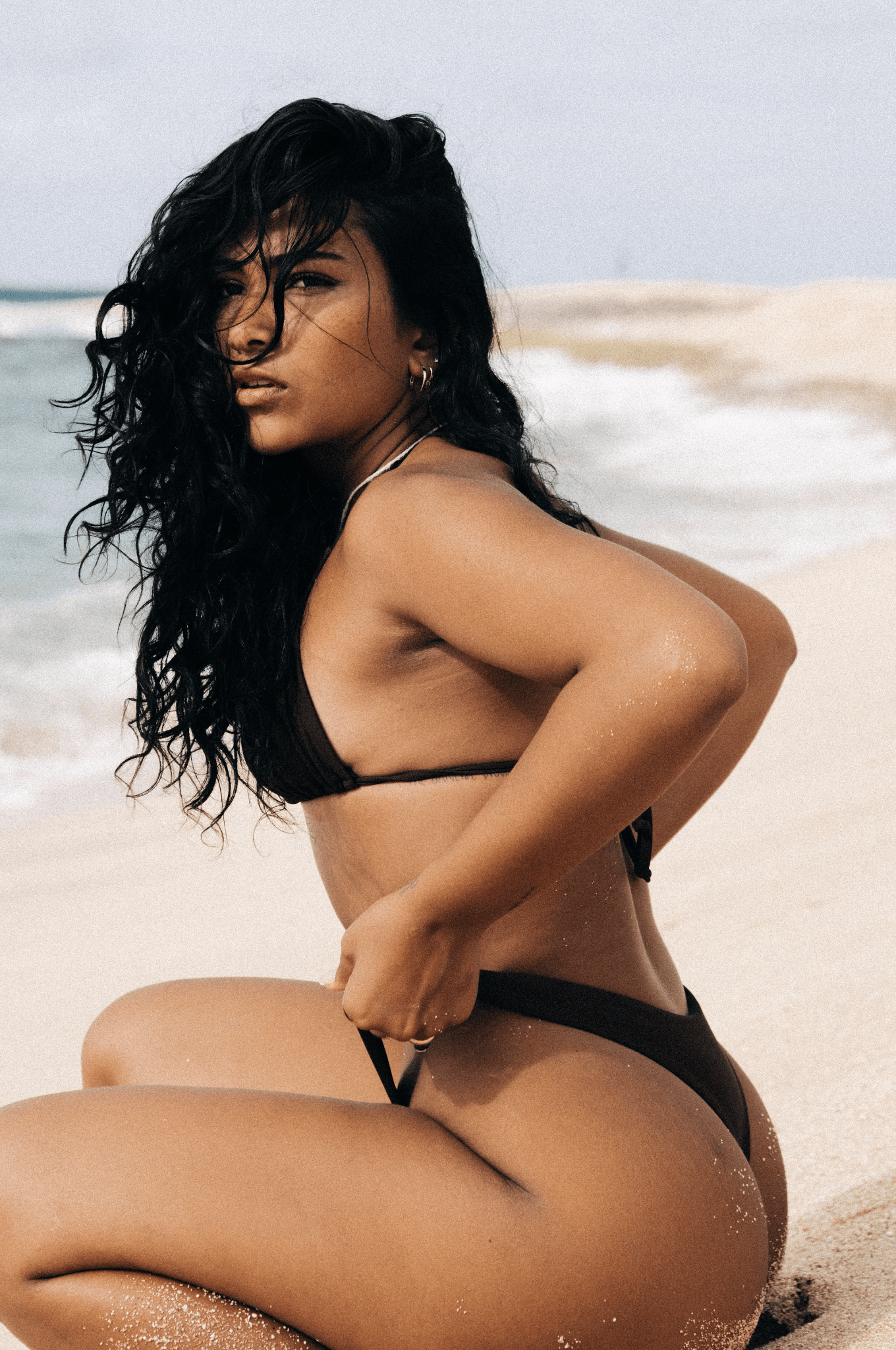 Girl kneeling beachside in the sand wearing brown bikini
