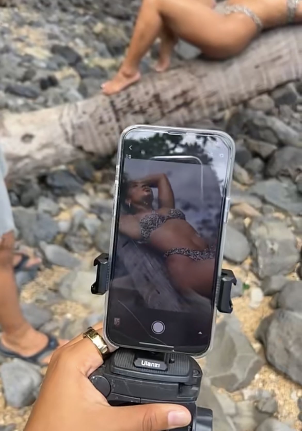 Photo of an iPhone taking a video of a girl in a bikini laying on a log