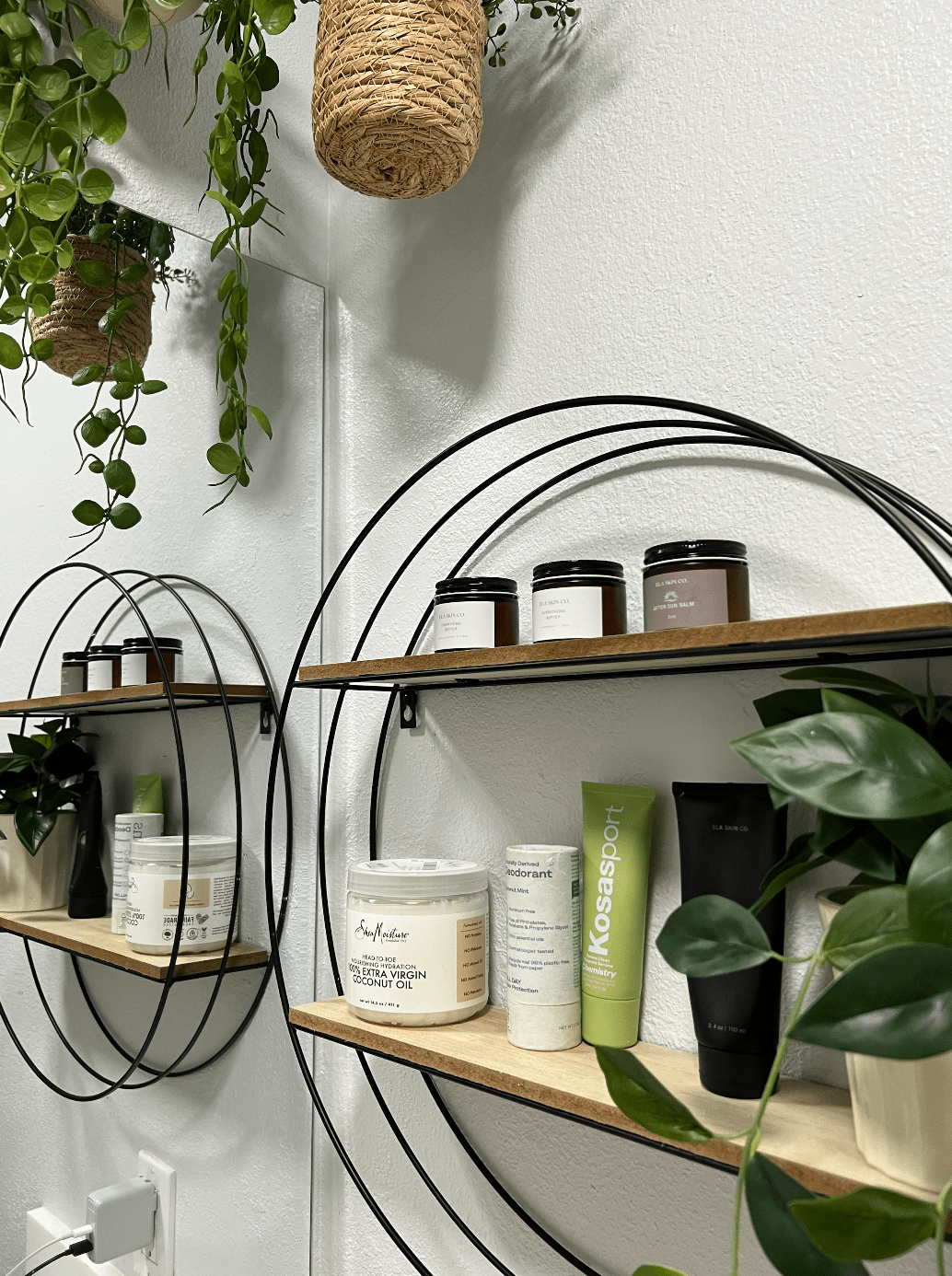 Various skincare products by Shea moisture, Ela Skin Co, Osea Malibu, and Kosas on circular shelf framed by plants