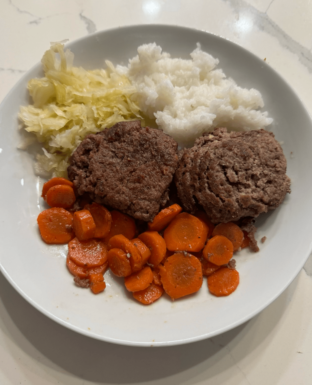 Beef patties, carrots, rice, and sauerkraut on a white plate