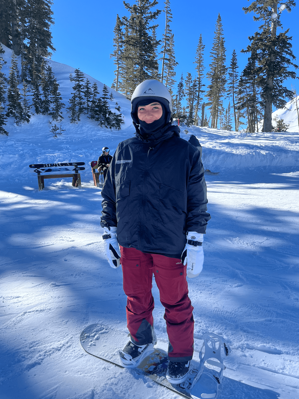 Girl in black jacket and red snow pants standing in snow on snowboard