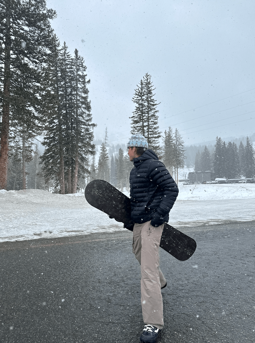 Boy in black jacket and beige pants holding snowboard on the street